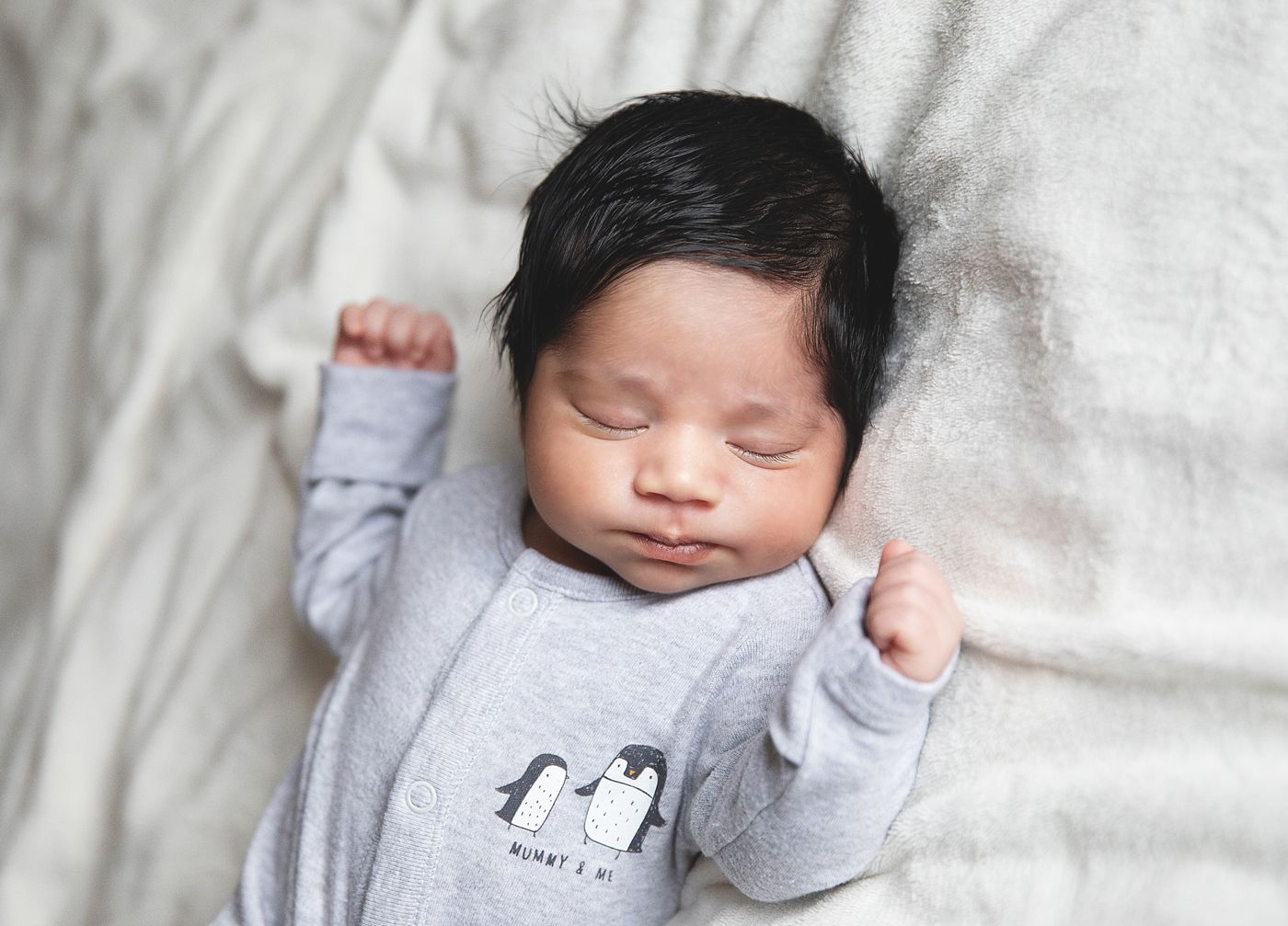 Black and white newborn portrait of a sleeping baby with dark hair, cradled in loving arms. During a home newborn session in Sidcup
