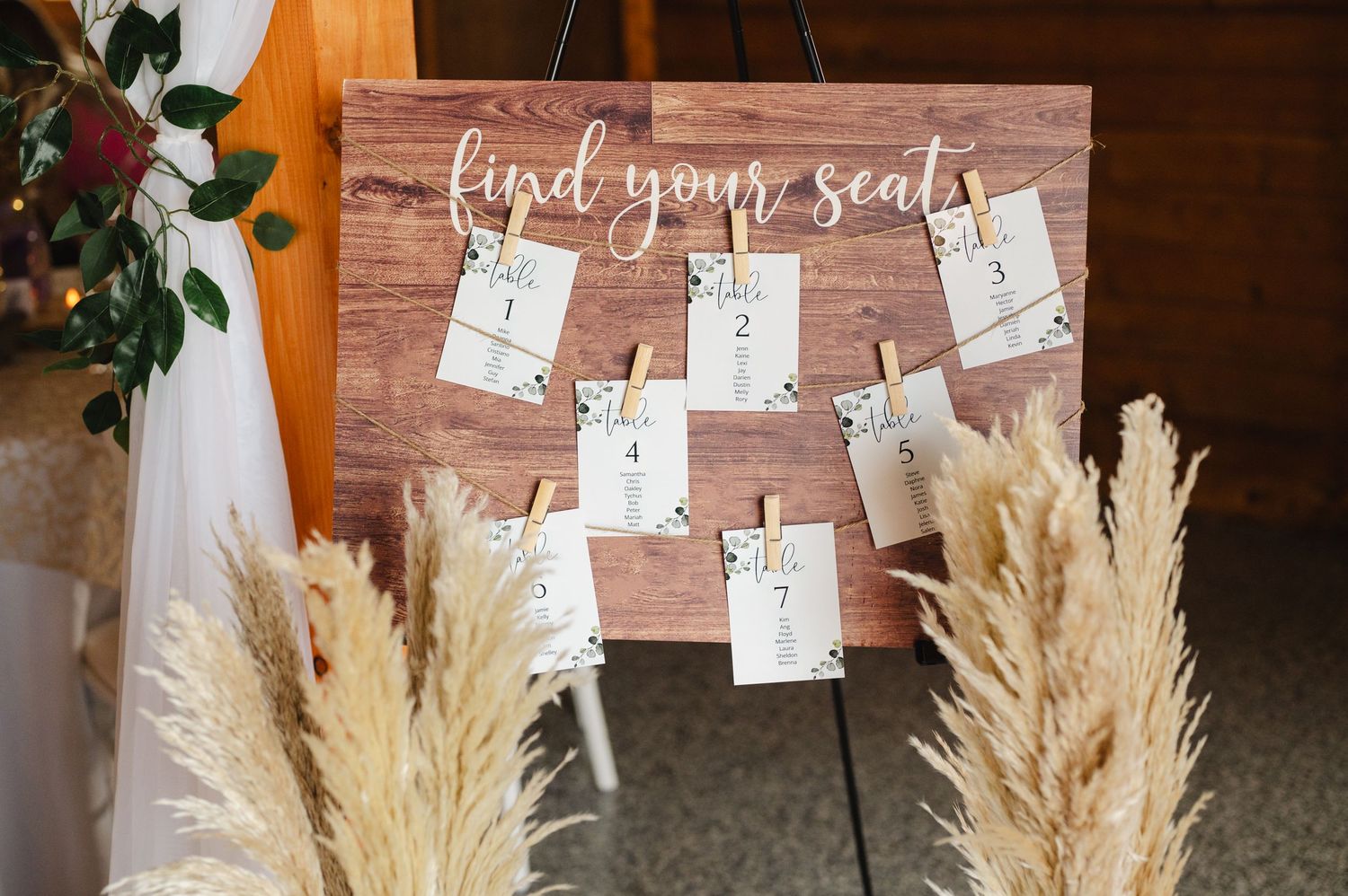 Rustic wooden wedding seating chart sign reading find your seat, decorated with pampas grass on an easel.