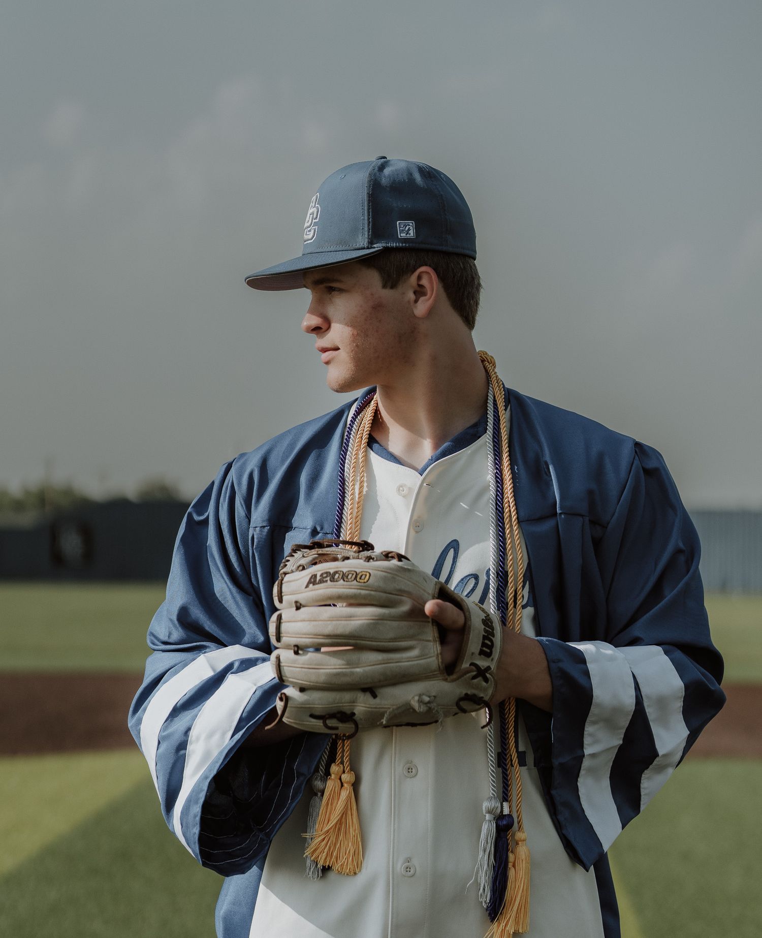 Athlete crouches at home plate on baseball field with stadium seating visible in background.