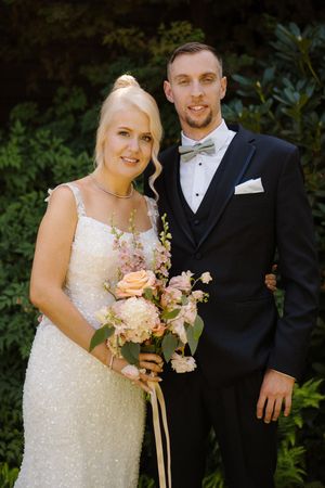 Bride in white sequin gown holding blush bouquet stands with groom in navy tuxedo outdoors.