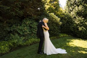 Bride and groom sharing a romantic kiss in a lush green garden, with the bride wearing an elegant white wedding gown.