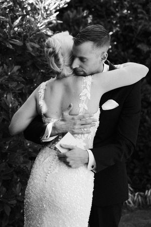 Black and white photo of a bride and groom sharing a tender embrace outdoors on their wedding day.