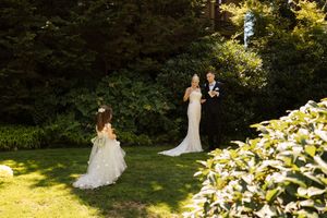 Bride and groom exchange vows outdoors in a sunlit garden, with a flower girl standing nearby.