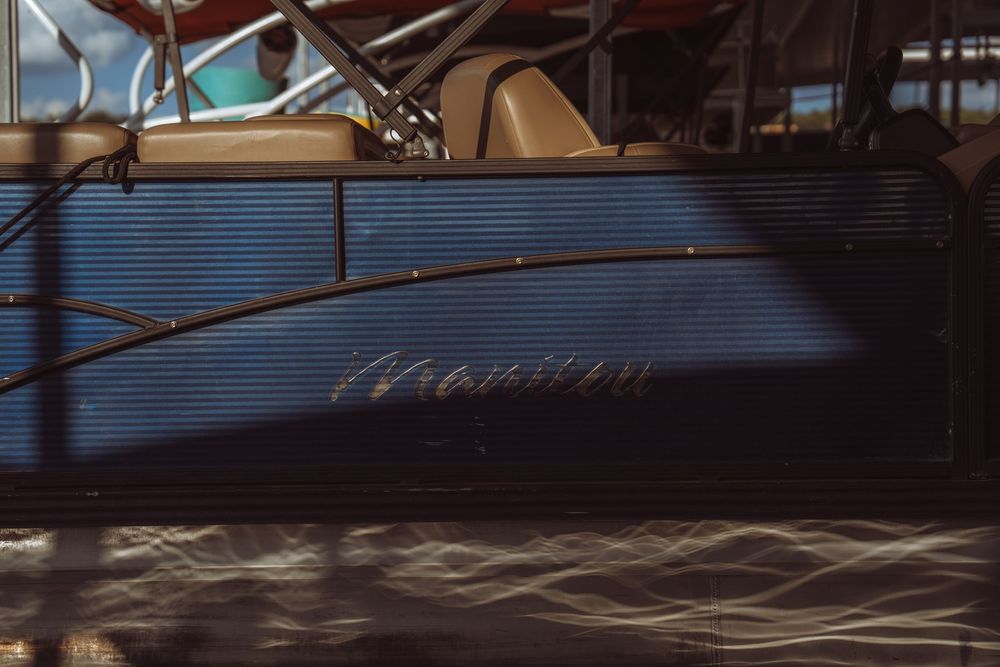 Close-up view of a blue pontoon boat docked at a marina, showcasing its sleek hull design in warm evening light.