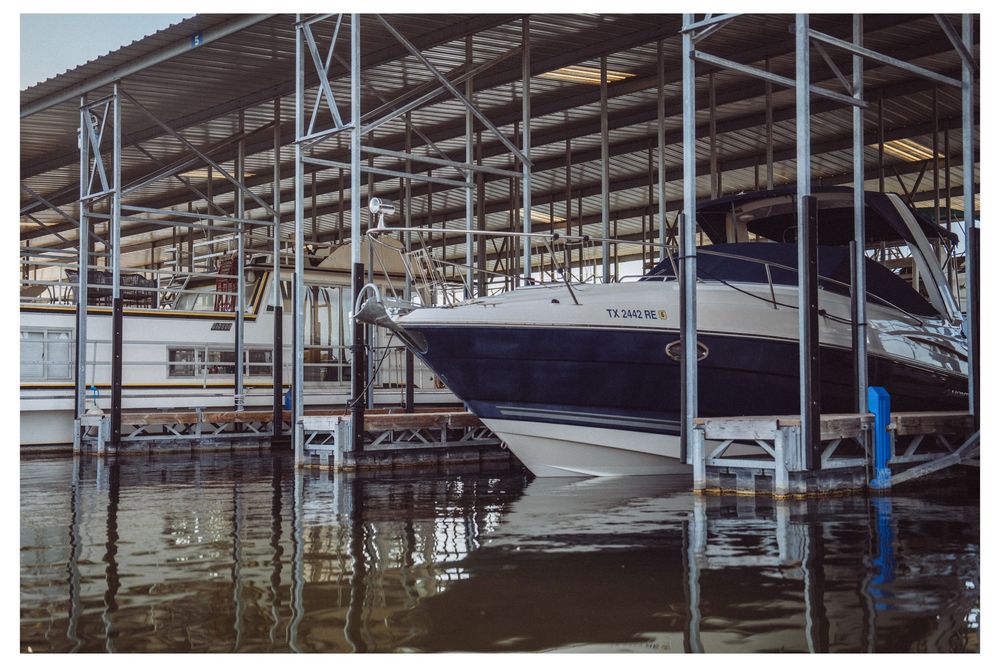 A large white motorboat docked in a covered marina slip with metal scaffolding over calm water.