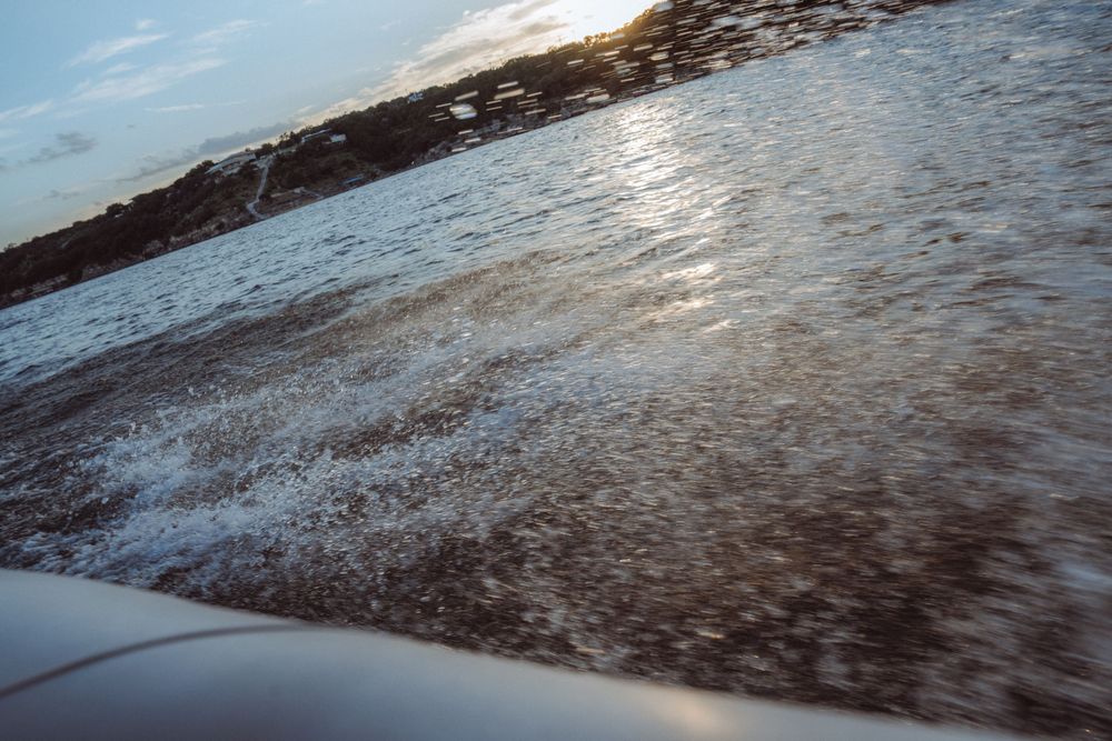 Aerial view of choppy ocean waves reflecting sunlight from a boat, with a distant shoreline at sunset.