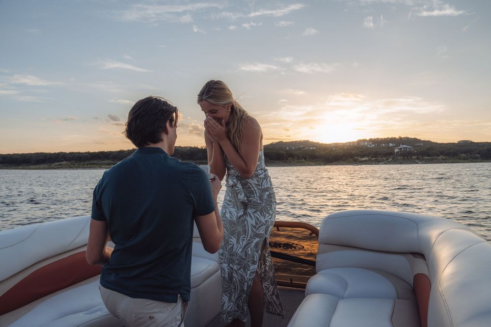 Couple sharing a romantic marriage proposal on a boat at sunset over calm water.