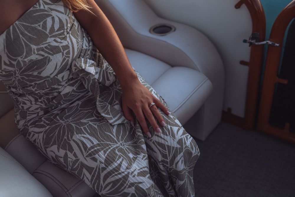 Woman in floral dress sitting on white leather boat seat with ring on hand.
