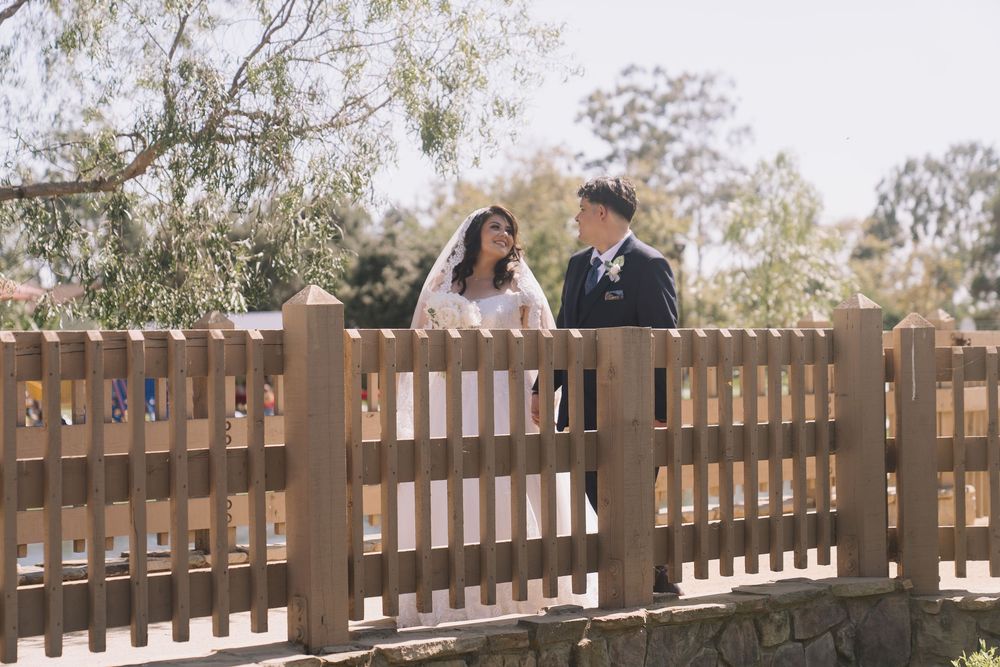 Bride and groom share a romantic moment standing behind a wooden fence at an outdoor wedding.