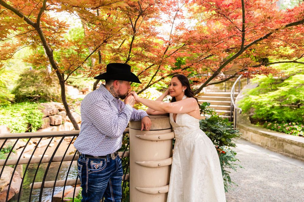 Bride and groom share a romantic moment by a stone pillar surrounded by vibrant autumn foliage in a garden.