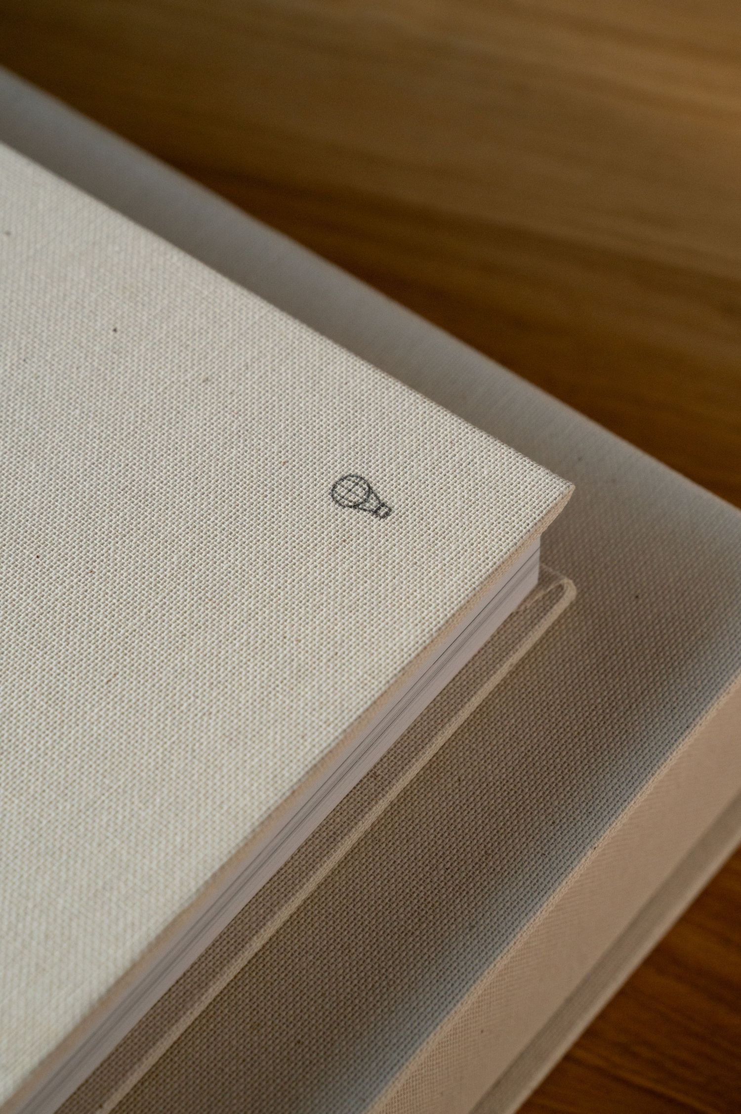 Close-up of a linen-covered wedding photo album with a small hot air balloon emblem on a wooden surface.