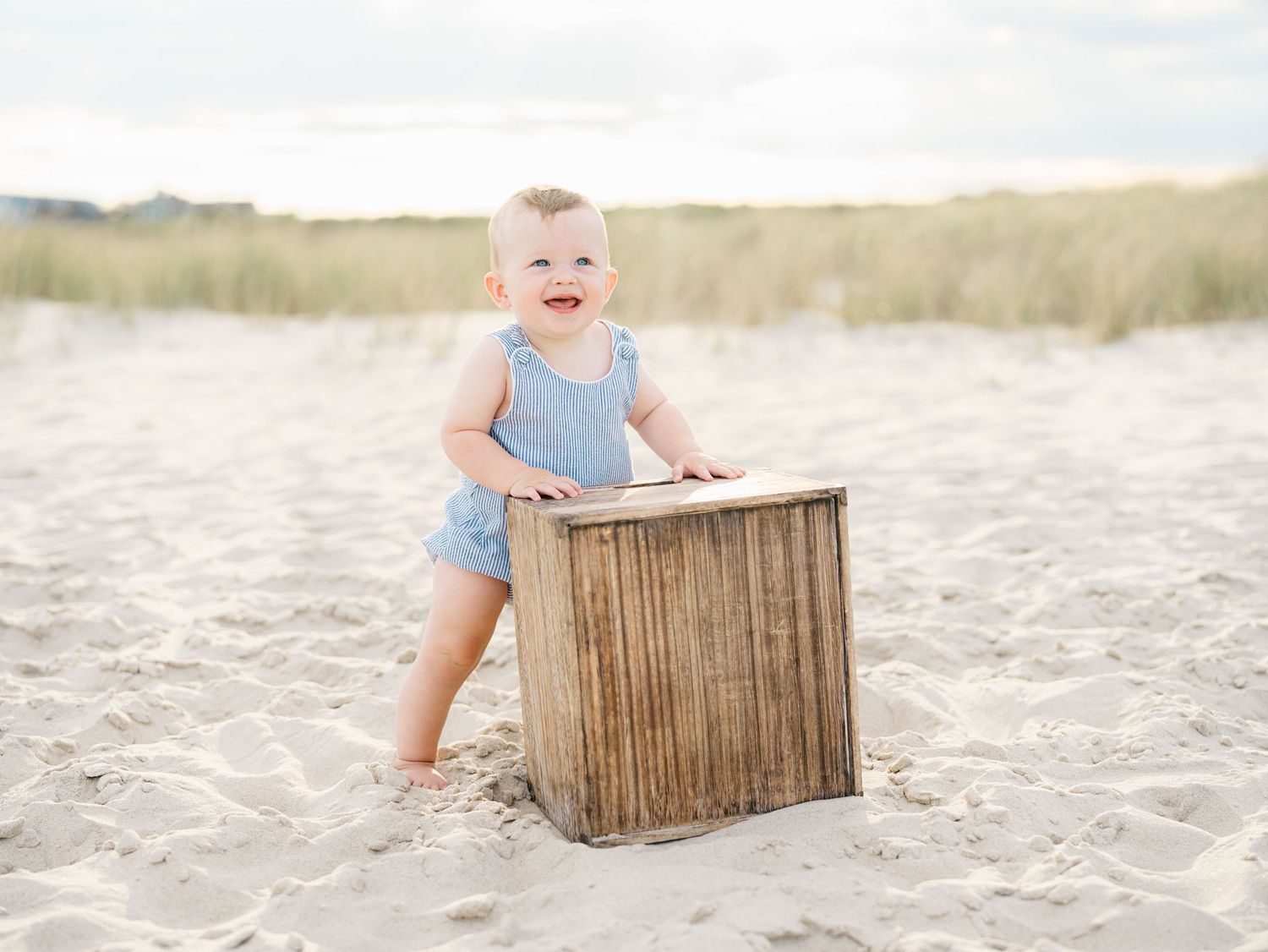Young toddler hold himself up on a wood crate on the jersey shore beach.