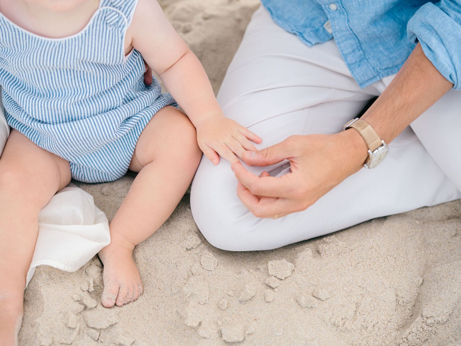 Close up image of father and son hands while sitting on the beach in monmouth county nj.