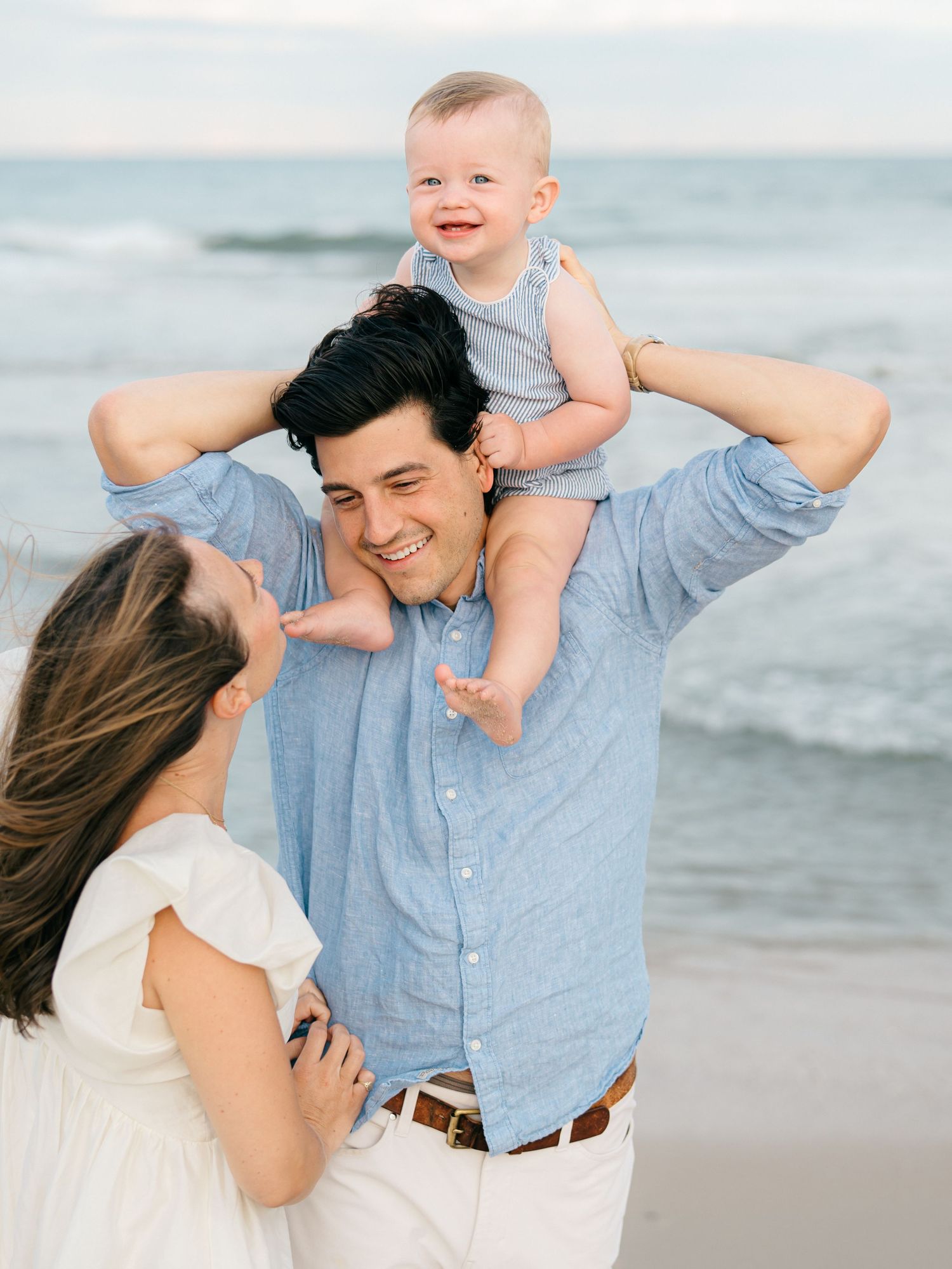 A father puts his toddler on his shoulders in front of the ocean on the nj beach.