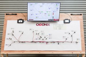 Cadonix smartBuild wiring harness diagram displayed on a large board with a monitor showing network layout above.