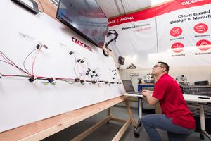 Engineer working at laptop beside circuit board display at Cadonix design and manufacturing booth.