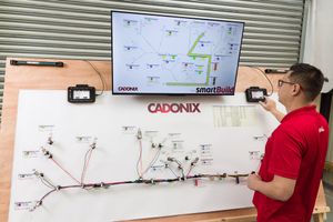 A man in a red shirt interacts with a Cadonix smartBuild wiring diagram display board and monitor.