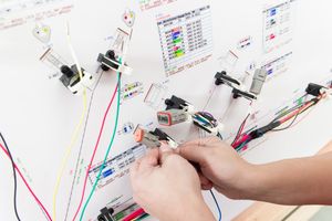 Hands connecting colorful wires to electronic components on a white board in an electronics lab setup.