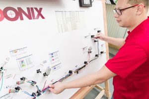 Technician in red shirt working on Cadonix electrical wiring panel board with multiple components and cables.