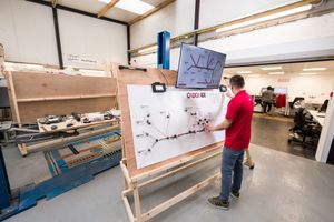 Engineer reviews network diagram on whiteboard beside monitor in industrial workshop setting.