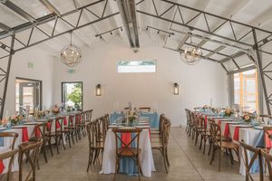 Elegant barn wedding reception hall with long tables, rustic wooden chairs, blue linens, and globe chandeliers.
