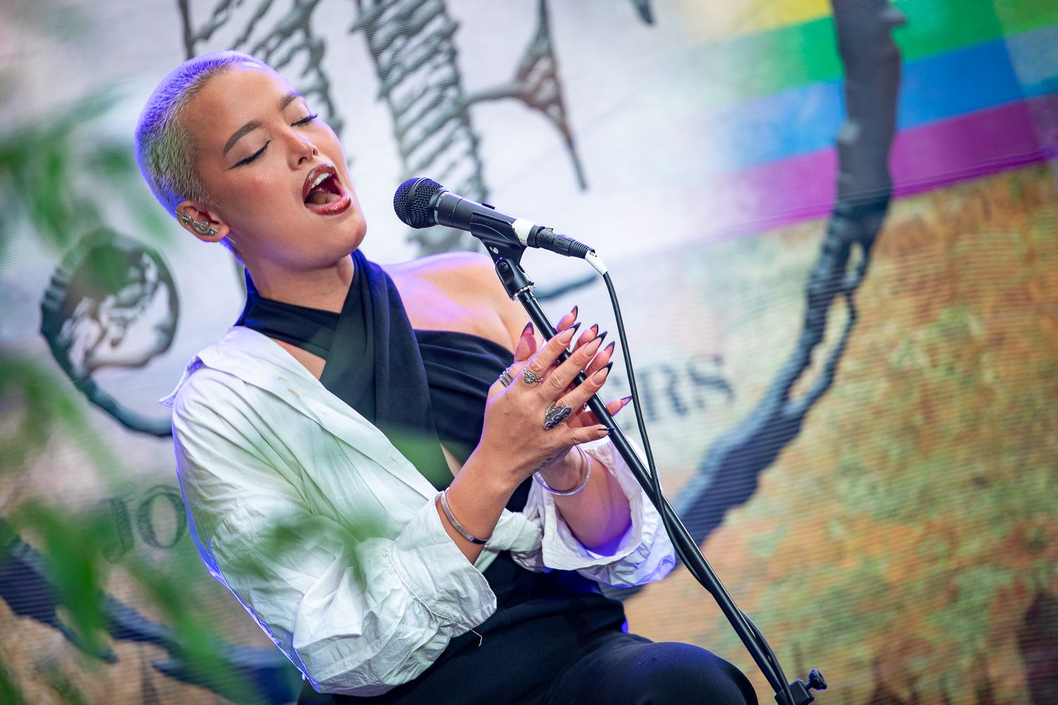 Young woman with short hair singing passionately into a microphone at an outdoor performance event.