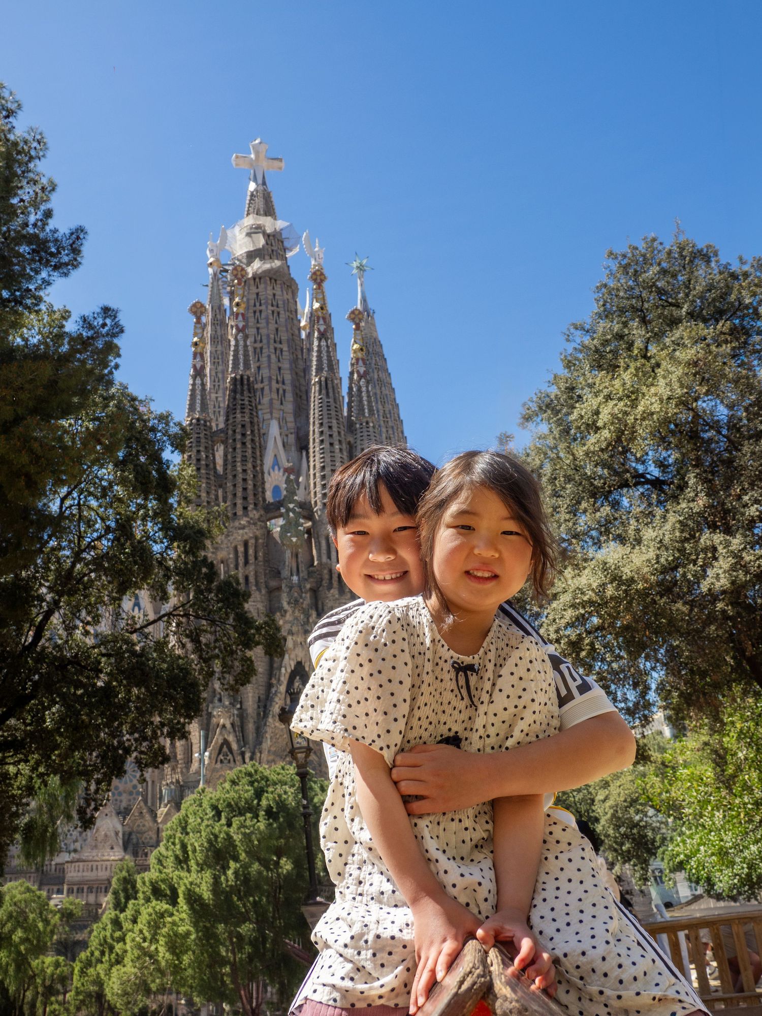 Two children smiling in front of Sagrada Familia basilica in Barcelona, Spain on a sunny day.