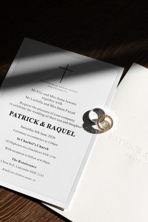 Wedding invitation for Patrick and Raquel with gold rings on wooden surface in natural light.