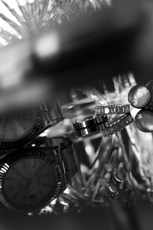 Black and white close-up of luxury watches and diamond wedding rings among pine branches.