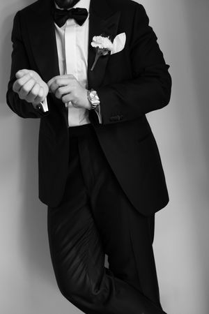 Black and white close-up of a groom in a tuxedo with boutonniere adjusting his cufflinks.