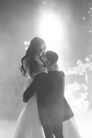 Black and white romantic first dance photo of smiling bride and groom surrounded by soft fog.
