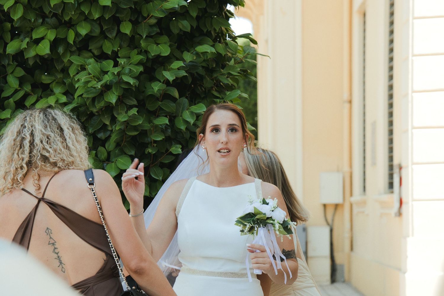 La mariée échange avec une proche à l’extérieur, son bouquet à la main.