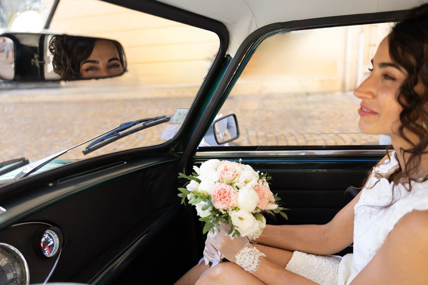 La mariée assise dans une voiture ancienne avec son bouquet de fleurs.