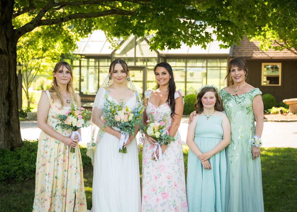 Five bridesmaids in floral and mint dresses holding bouquets pose outdoors at a garden wedding venue.