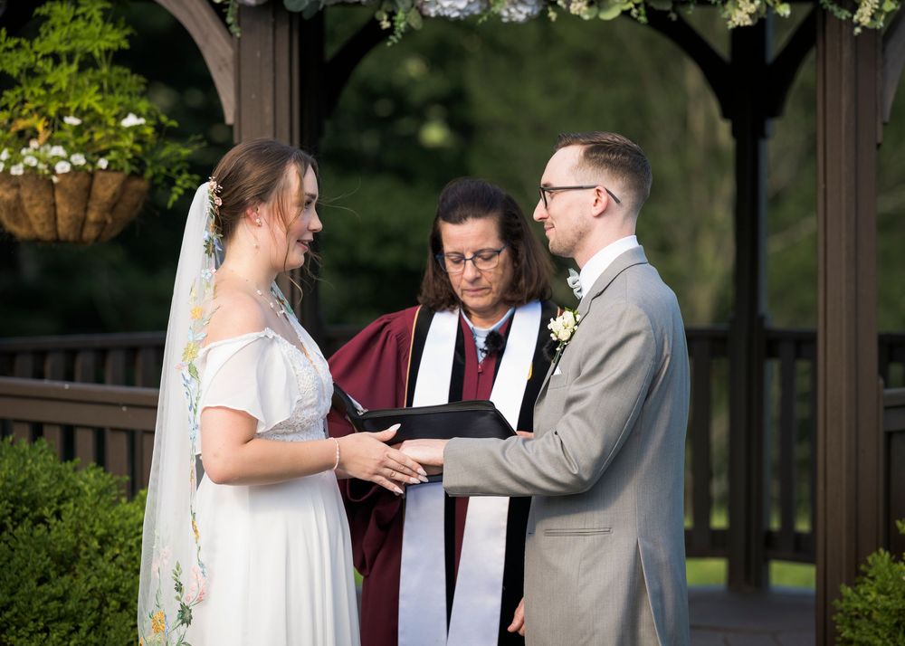 Bride and groom exchange vows with officiant under floral gazebo at outdoor wedding ceremony.