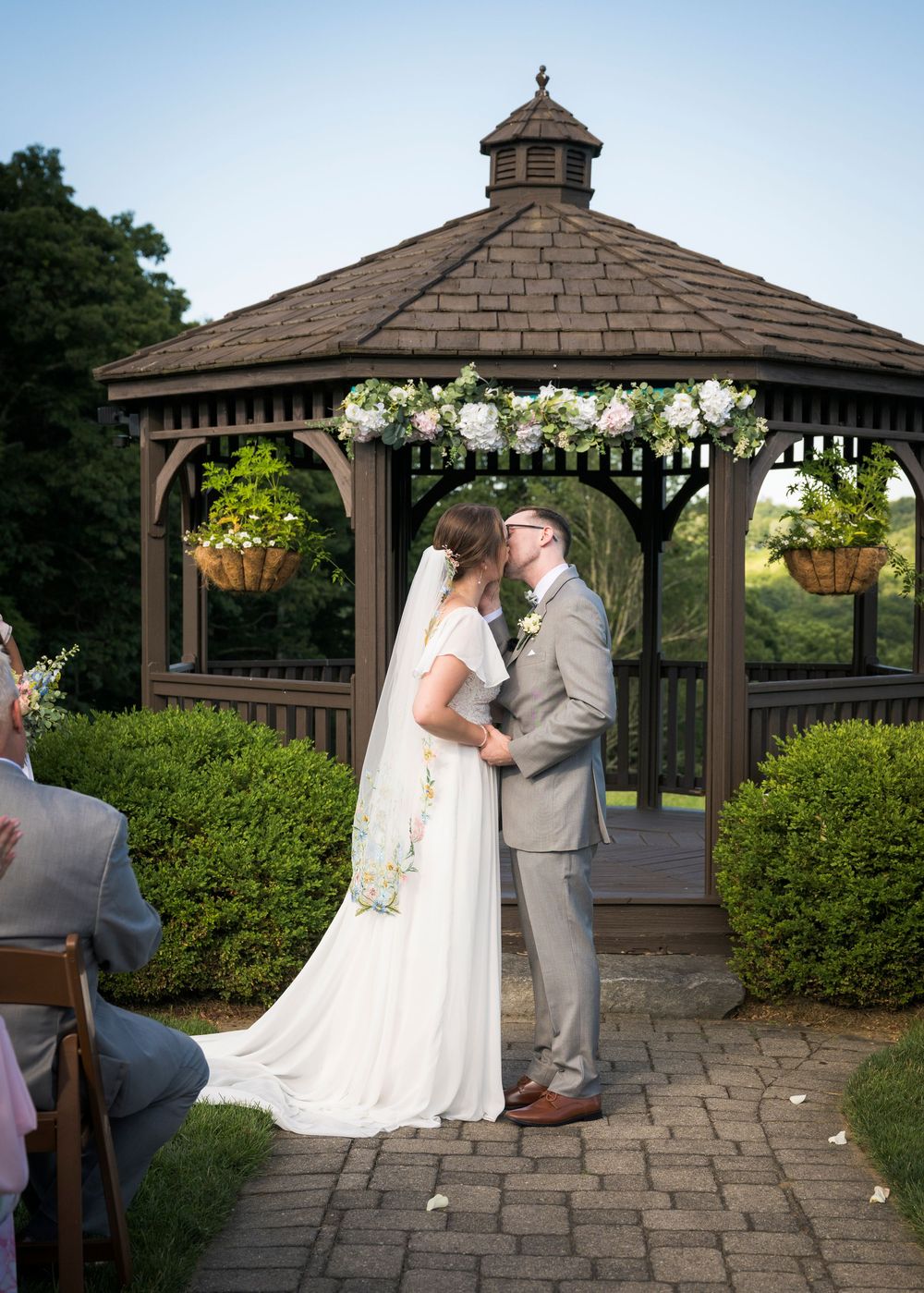 Bride and groom sharing a first kiss under a decorated gazebo during an outdoor wedding ceremony.