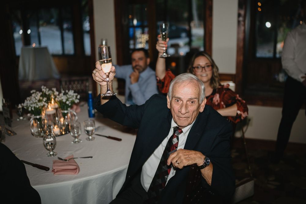 Elderly man in suit raising a champagne glass toast at an elegant wedding reception dinner.