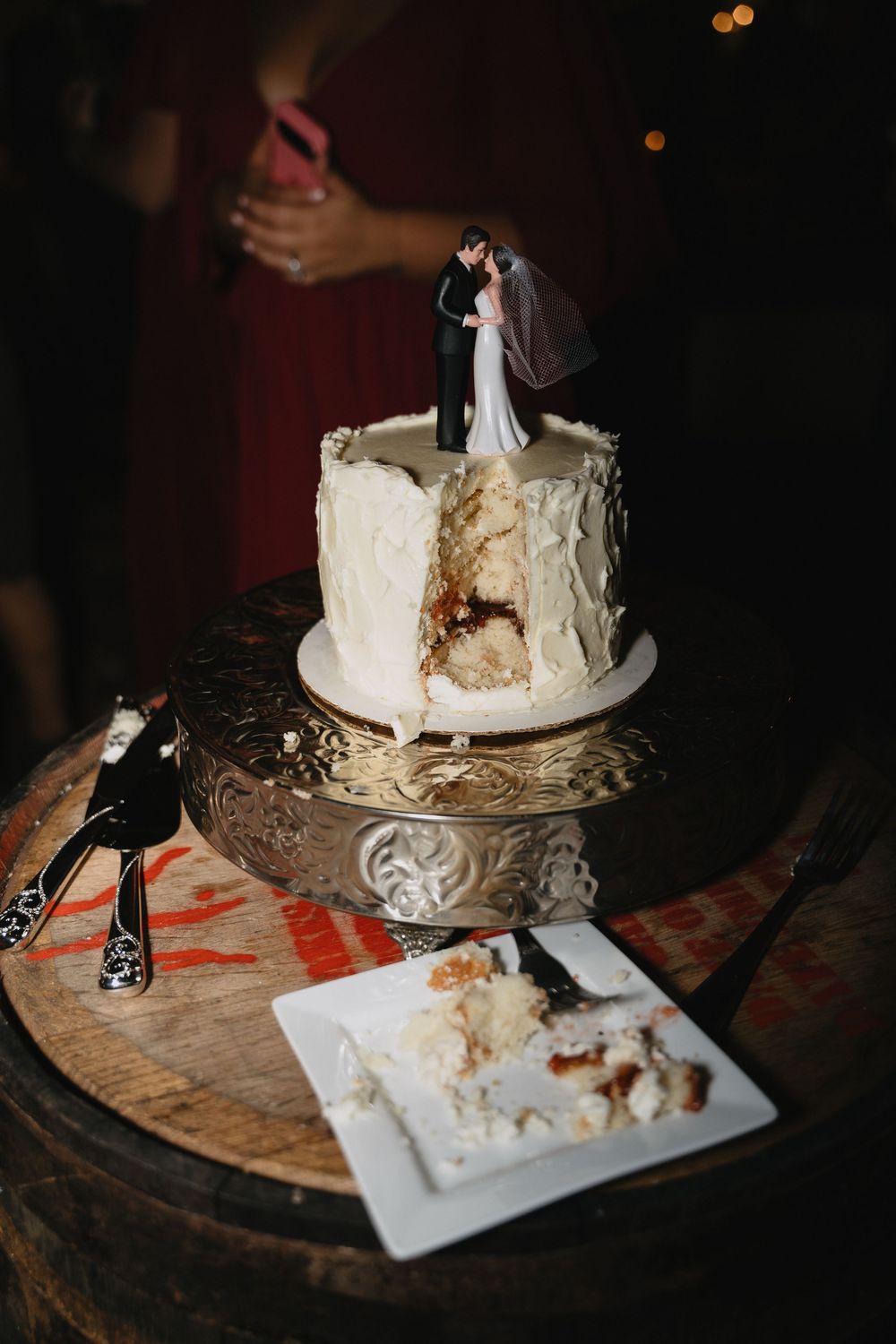 Single-tier white wedding cake with bride and groom topper on silver stand, slice removed revealing layers inside.