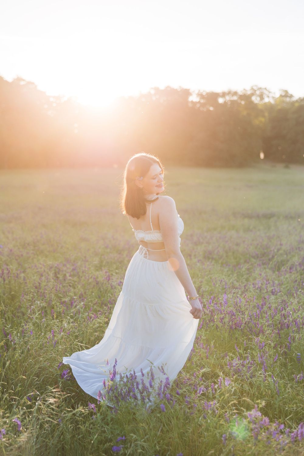 Woman in white dress standing in a sunlit lavender field at golden hour, glancing back over her shoulder.