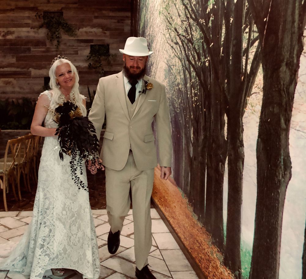 Bride in blue lace gown and groom in beige suit walk together at indoor wedding venue.