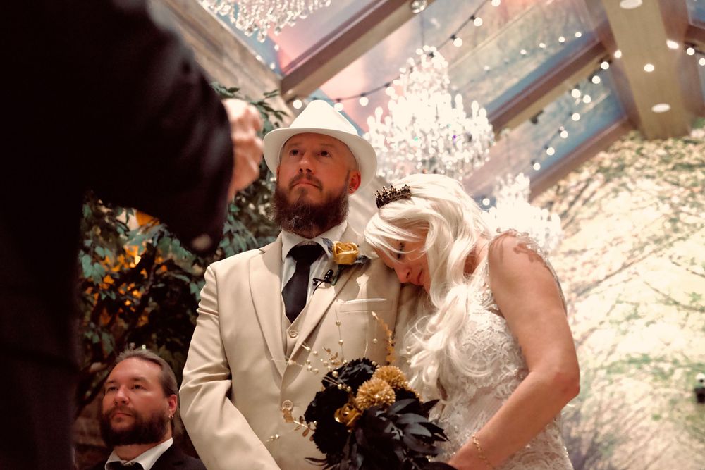 Bride and groom exchange vows under sparkling chandelier at elegant indoor wedding ceremony with guests.
