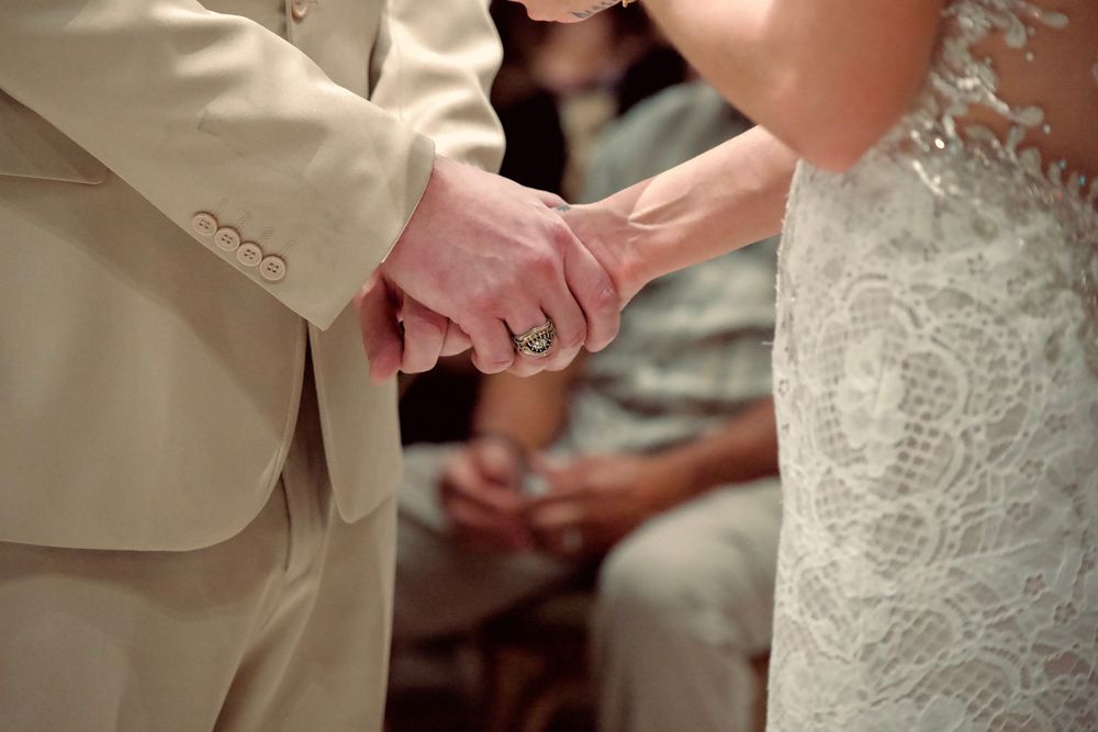 Close-up of bride and groom holding hands during wedding ceremony, showcasing elegant rings.