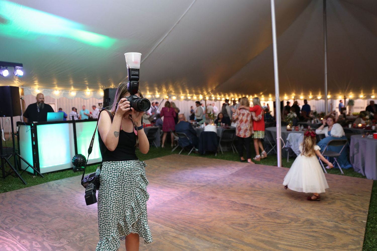 Photographer capturing moments at an elegant outdoor wedding reception under a white tent with string lights.