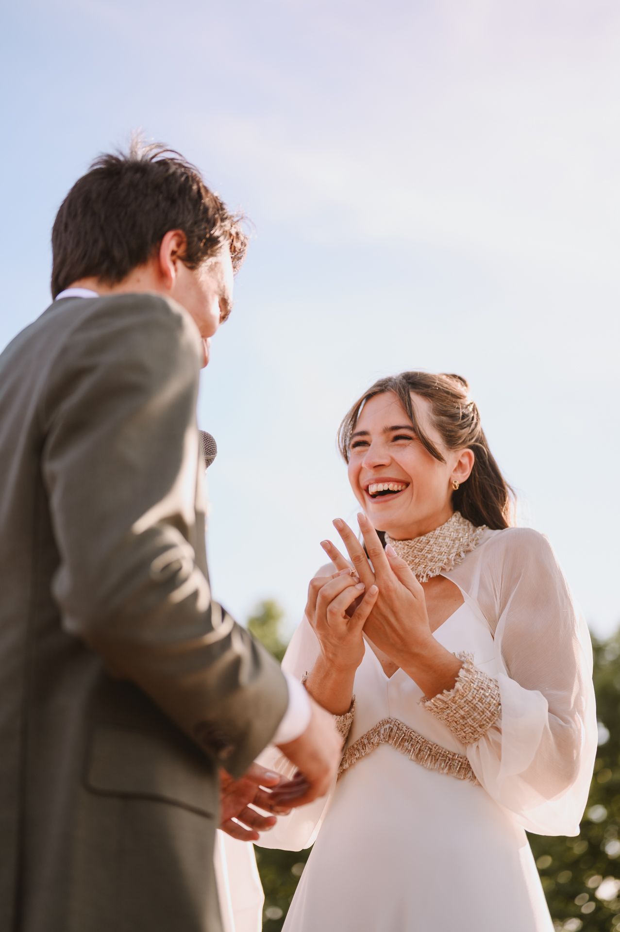 Laughing bride showing her ring to groom during outdoor wedding ceremony.