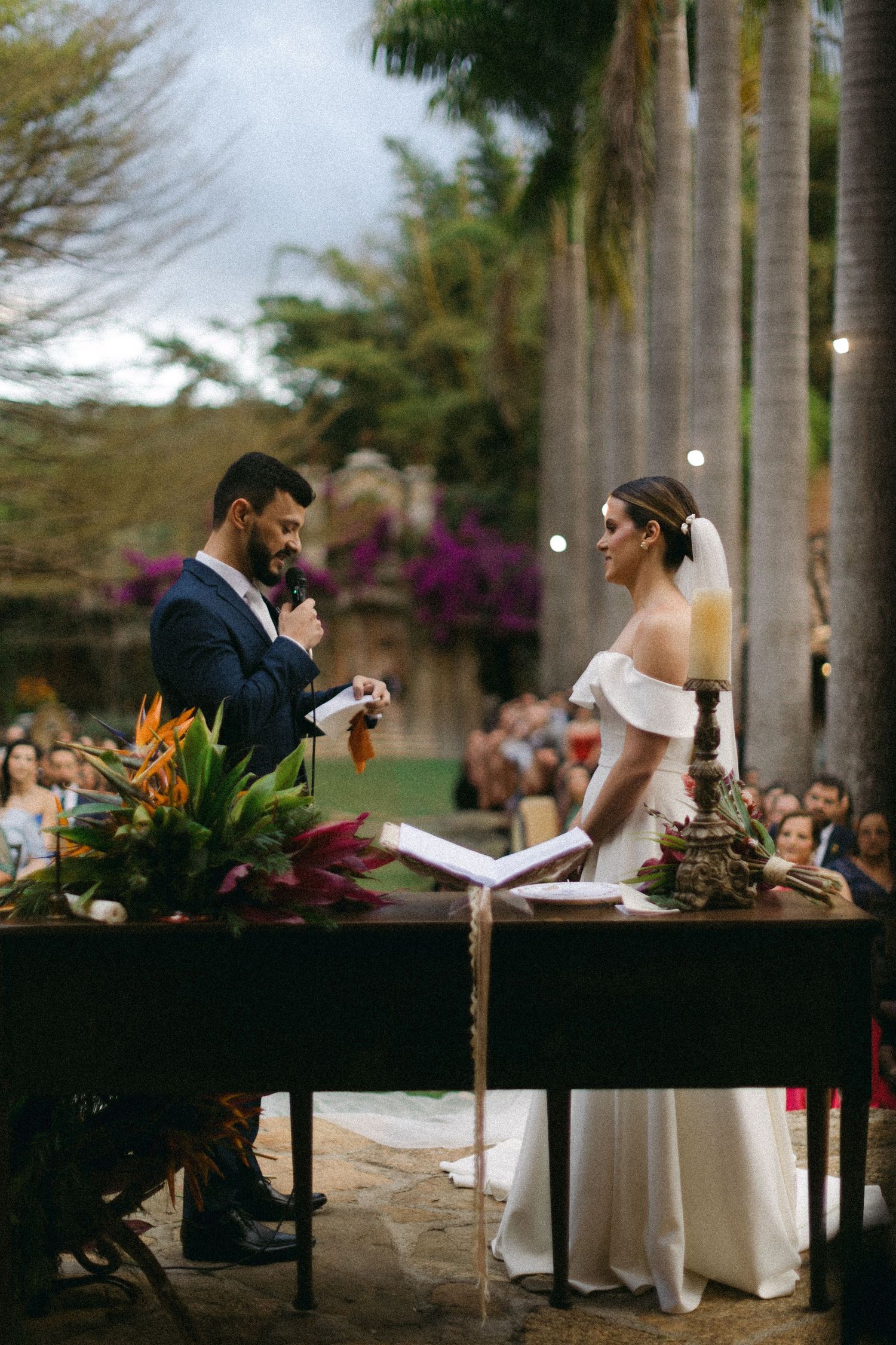 Wedding ceremony under palm trees in a tropical garden setting with decorative flowers and foliage.