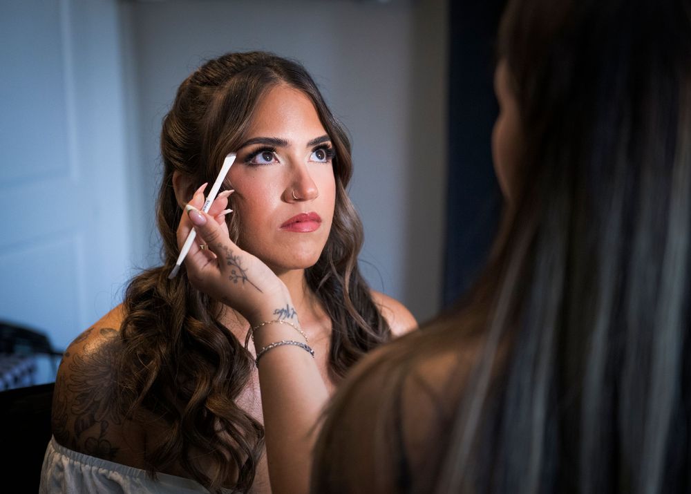 Bride getting makeup applied before her wedding ceremony, featuring elegant curled hair and a delicate necklace.