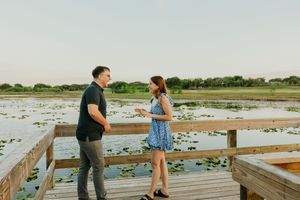 A couple shares a romantic moment on a wooden boardwalk overlooking a serene lily pad lake.
