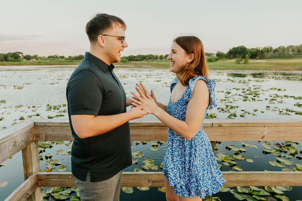 Couple sharing joyful reaction moment on wooden dock overlooking lily pad covered lake at sunset.