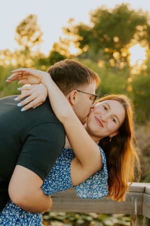 A man kisses a smiling woman on the cheek during a golden hour engagement photo session outdoors.