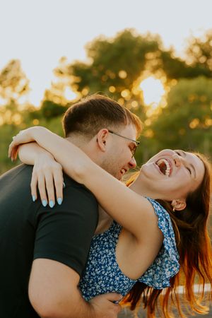 A laughing woman is lifted by her partner during a warm golden hour outdoor engagement session.